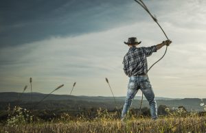 A farmer in his field with his lasso ready to lace a cow.
