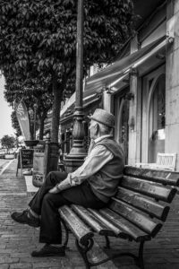 Black and white image of an elderly man sitting on a park bench. Loneliness and sadness.